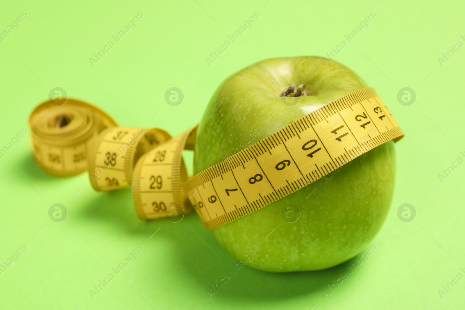 Photo of Weight loss concept. Apple and measuring tape on green background, closeup with space for text