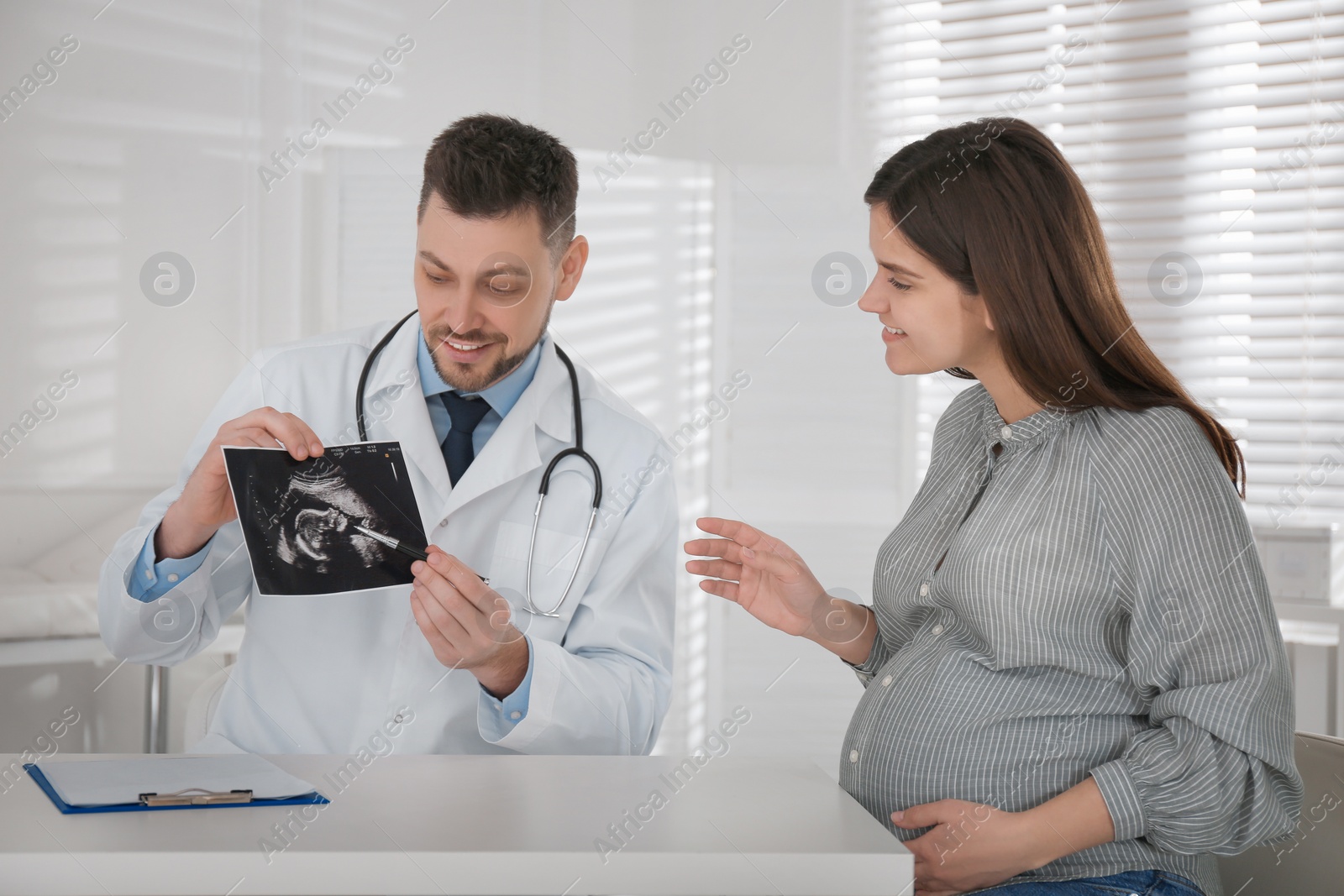 Photo of Gynecologist showing ultrasound picture to pregnant woman in clinic