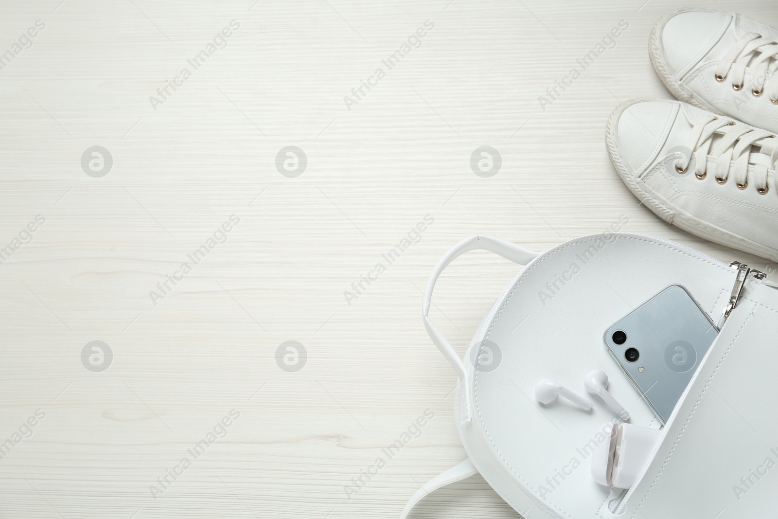 Photo of Backpack, sneakers, mobile phone and earphones on white wooden background, above view. Space for text