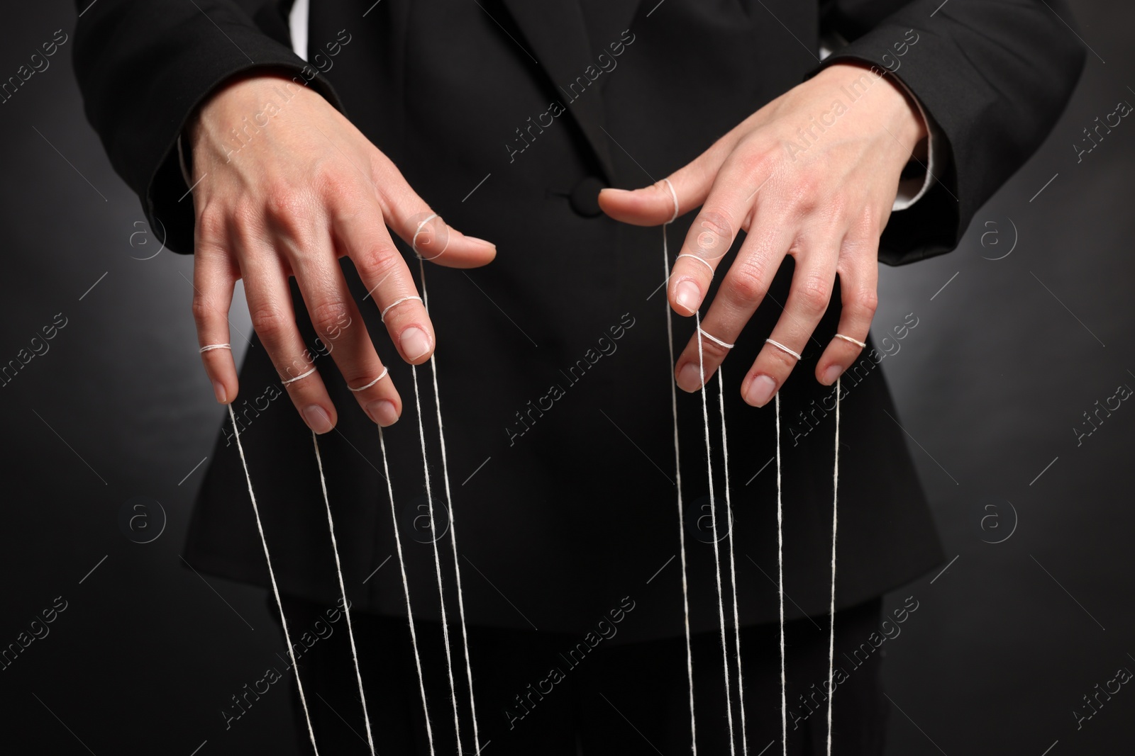 Photo of Woman in suit pulling strings of puppet on dark background, closeup