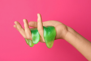 Photo of Woman playing with green slime on pink background, closeup. Antistress toy