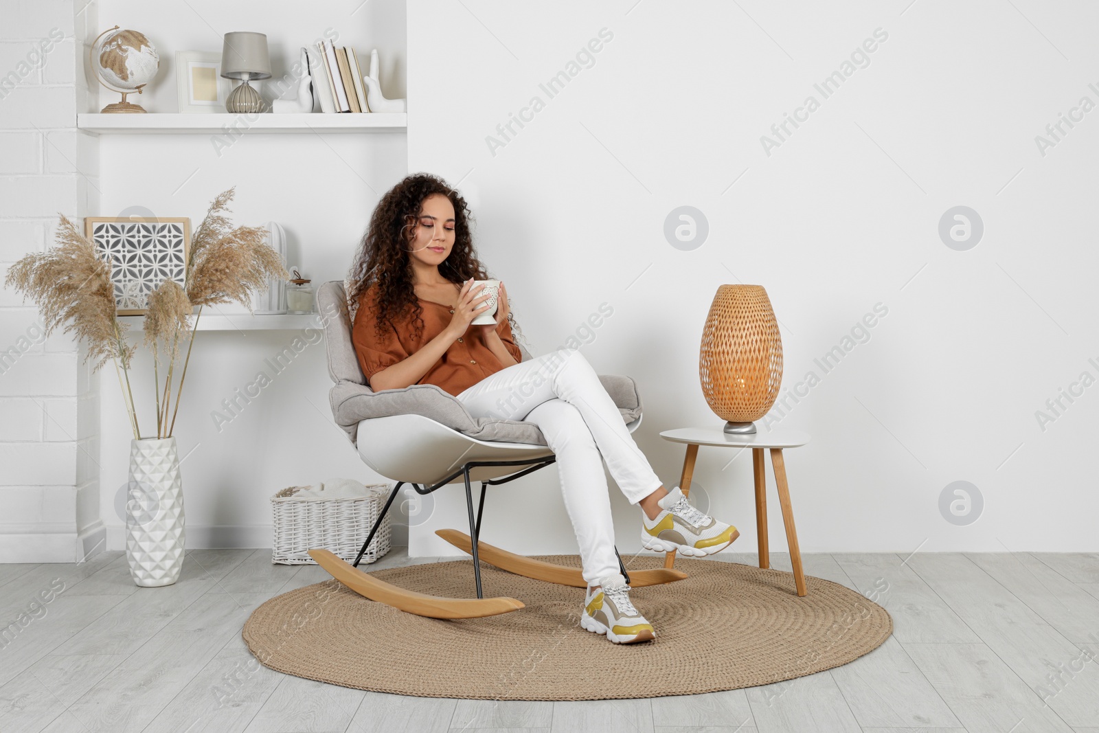 Photo of Young African-American woman with cup of drink sitting in rocking chair at home