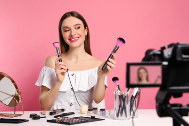 Photo of Beauty blogger recording makeup tutorial on pink background