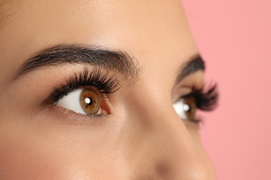 Beautiful young woman with long eyelashes on pink background, closeup