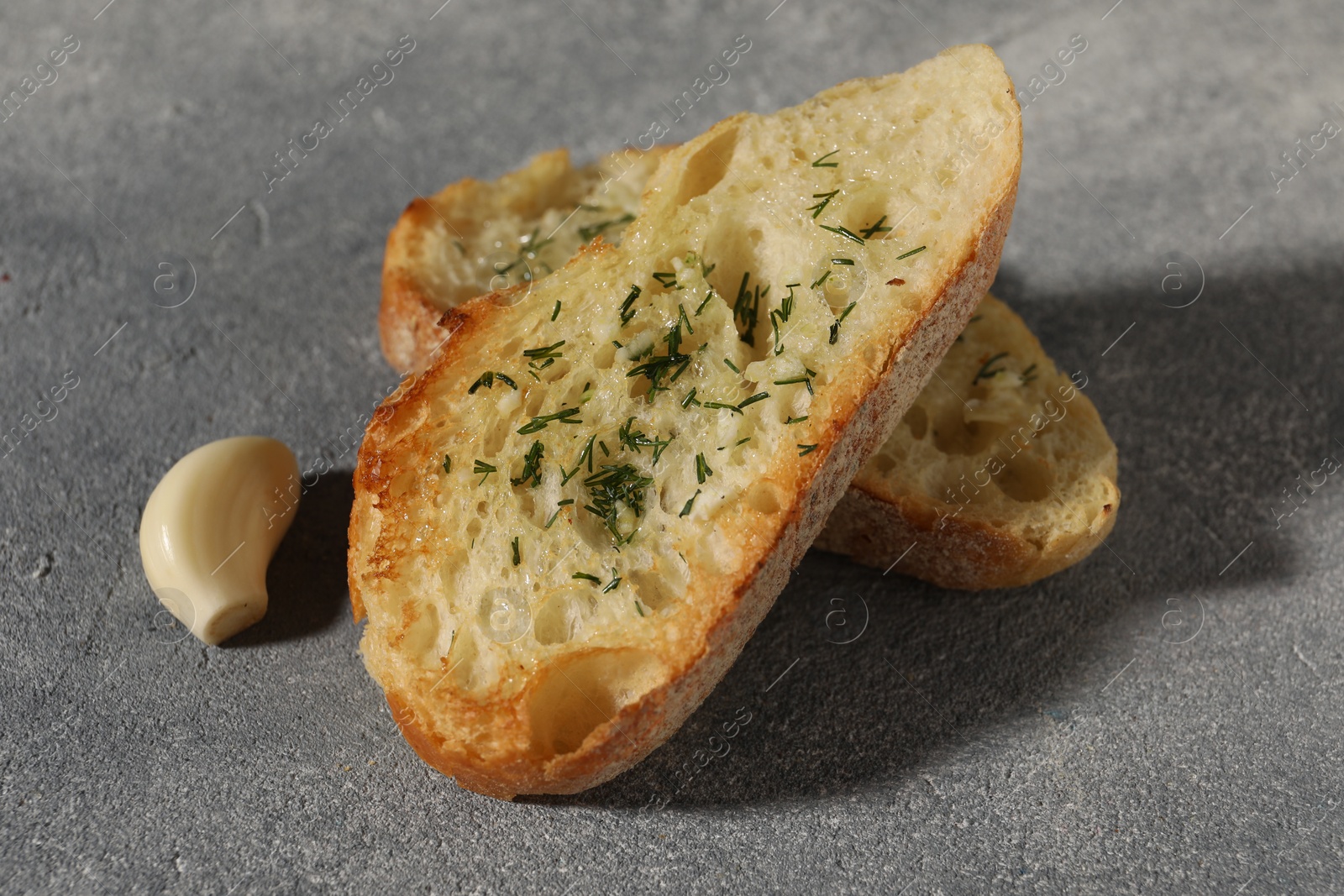 Photo of Tasty baguette with garlic and dill on grey textured table, closeup