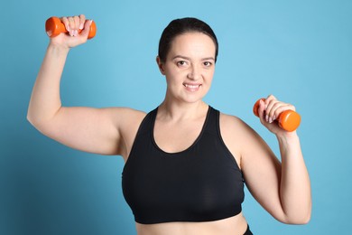 Photo of Happy overweight woman doing exercise with dumbbells on light blue background