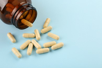 Bottle and vitamin capsules on light blue background, closeup. Space for text