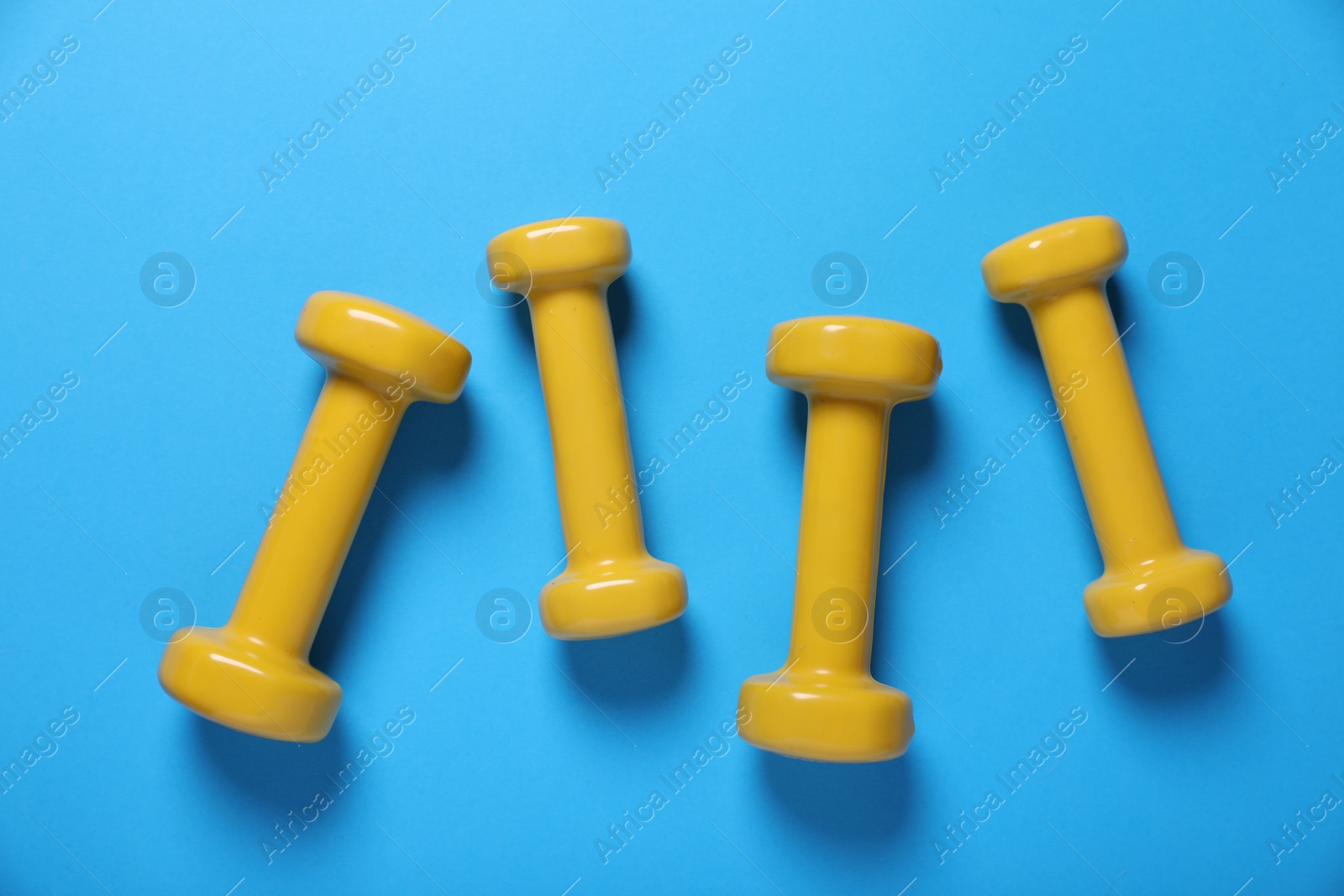 Photo of Yellow dumbbells on light blue background, flat lay. Morning exercise