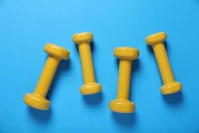 Yellow dumbbells on light blue background, flat lay. Morning exercise