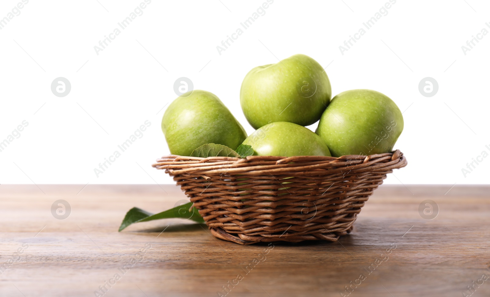 Photo of Ripe green apples in wicker basket on wooden table against white background