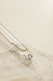 Photo of Dripping cosmetic oil from pipette onto beige background, closeup. Space for text