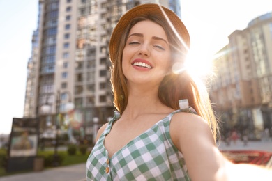 Beautiful young woman in stylish hat taking selfie outdoors