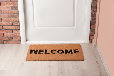 Door mat with word Welcome on wooden floor in hall