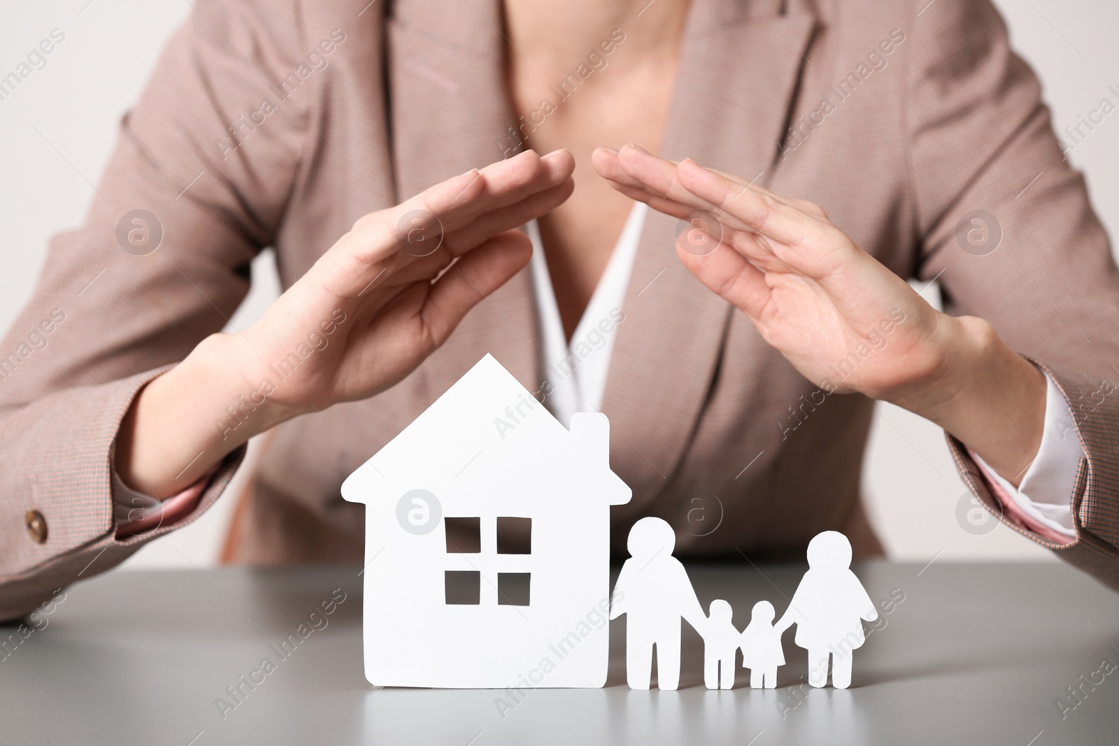 Photo of Female agent covering house model and family at table, closeup. Home insurance