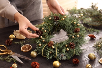 Florist making beautiful Christmas wreath at wooden table indoors, closeup