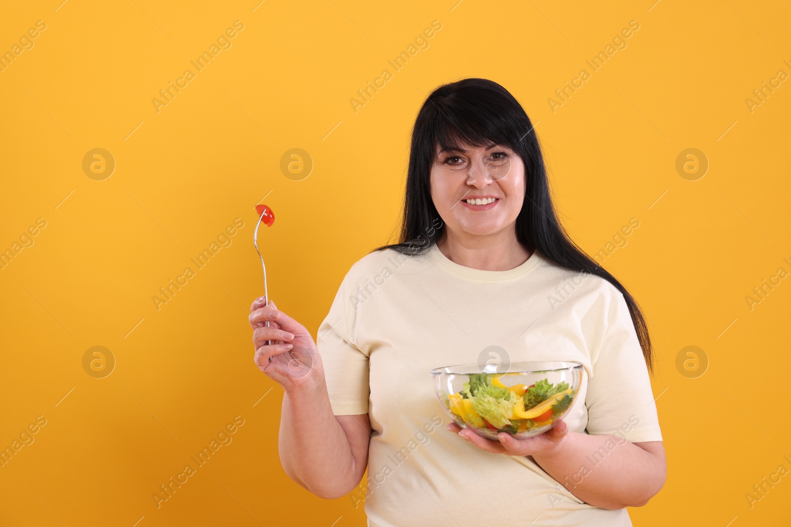 Photo of Beautiful overweight woman eating salad on yellow background, space for text. Healthy diet