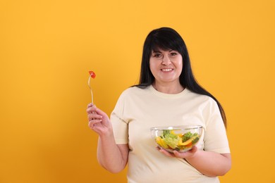 Beautiful overweight woman eating salad on yellow background, space for text. Healthy diet