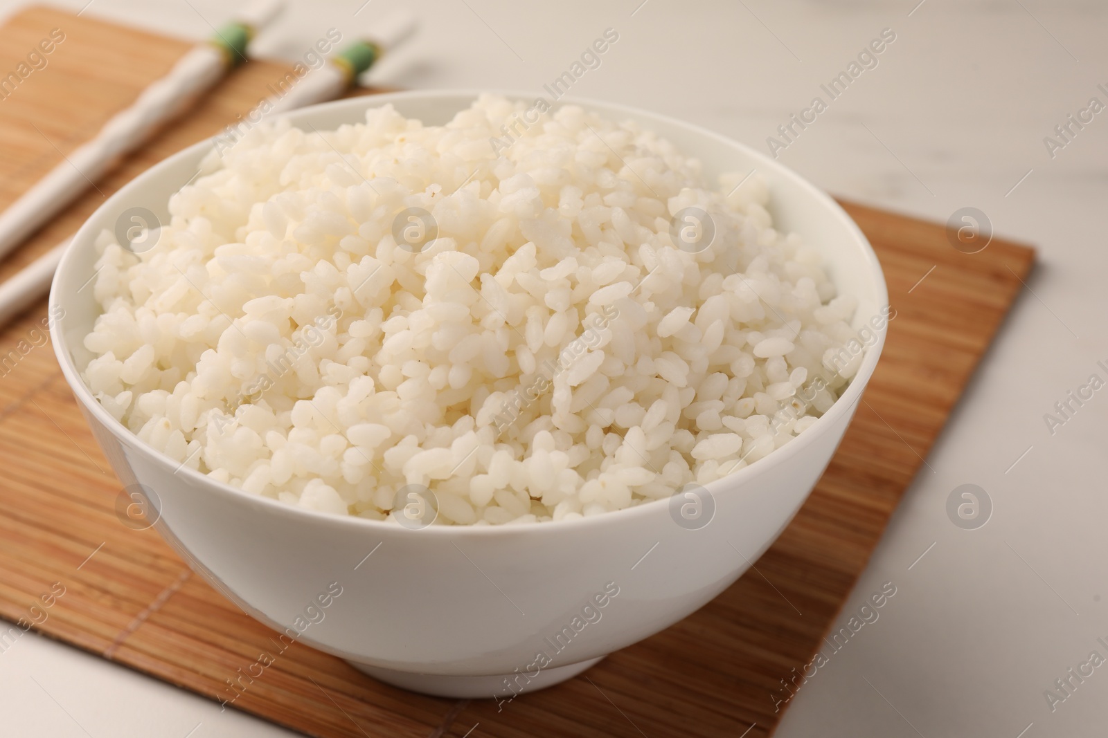 Photo of Bowl with delicious rice and chopsticks on white table, closeup