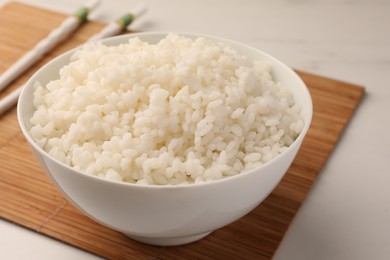 Photo of Bowl with delicious rice and chopsticks on white table, closeup