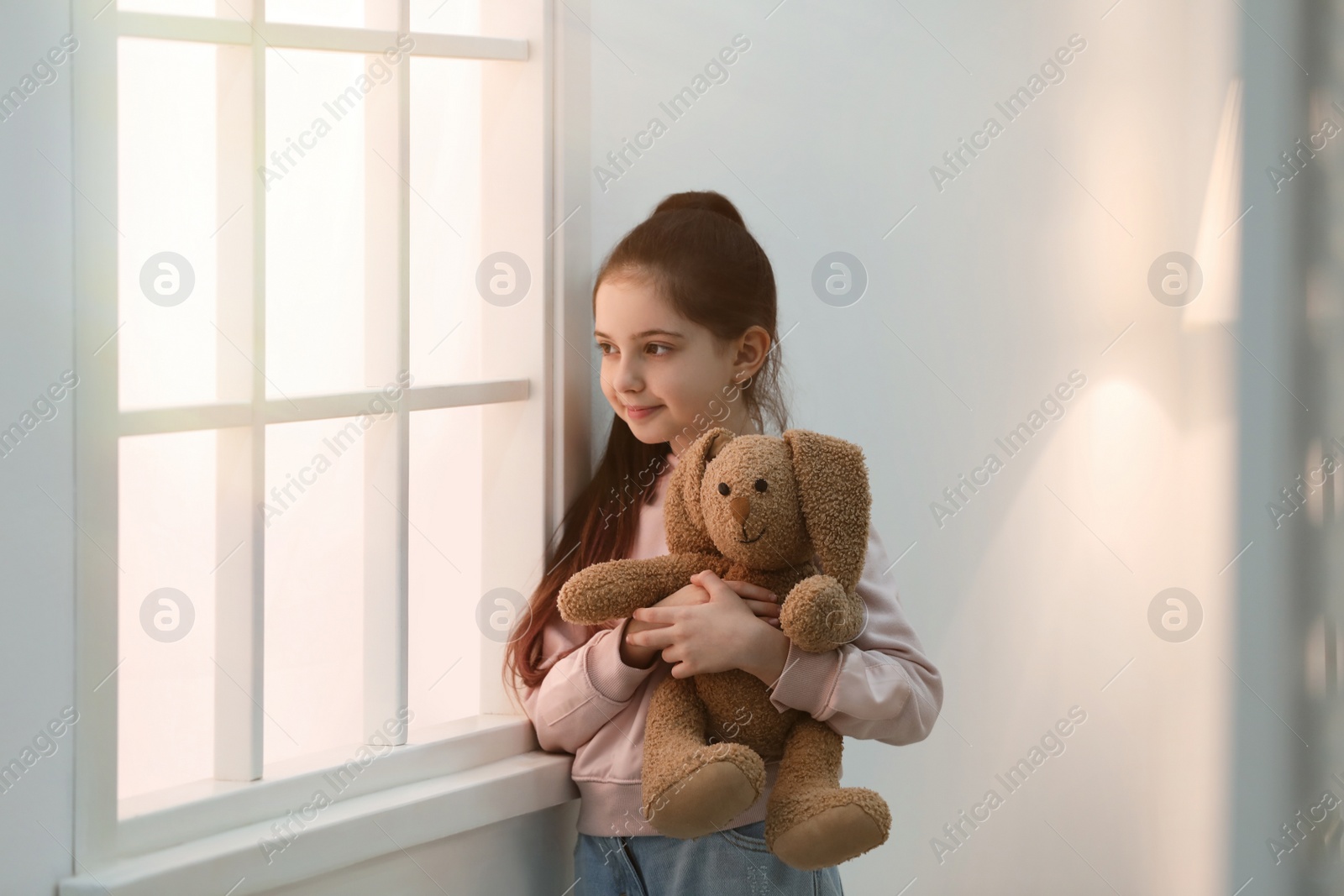 Photo of Cute little girl with toy near window at home