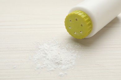 Bottle and scattered dusting powder on white wooden background. Baby cosmetic product