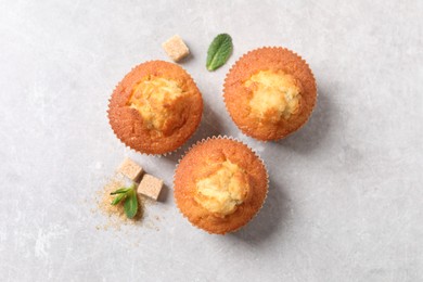 Delicious sweet muffins and brown sugar on light grey textured table, flat lay