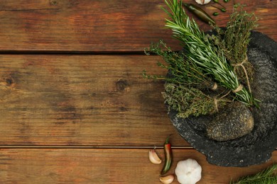 Photo of Mortar, different herbs and vegetables on wooden table, flat lay. Space for text