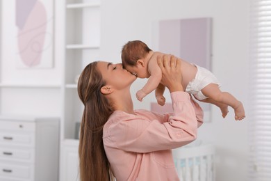 Photo of Mother kissing her cute newborn baby in child's room
