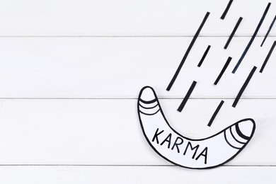 Paper boomerang with word Karma on white wooden table, flat lay. Space for text