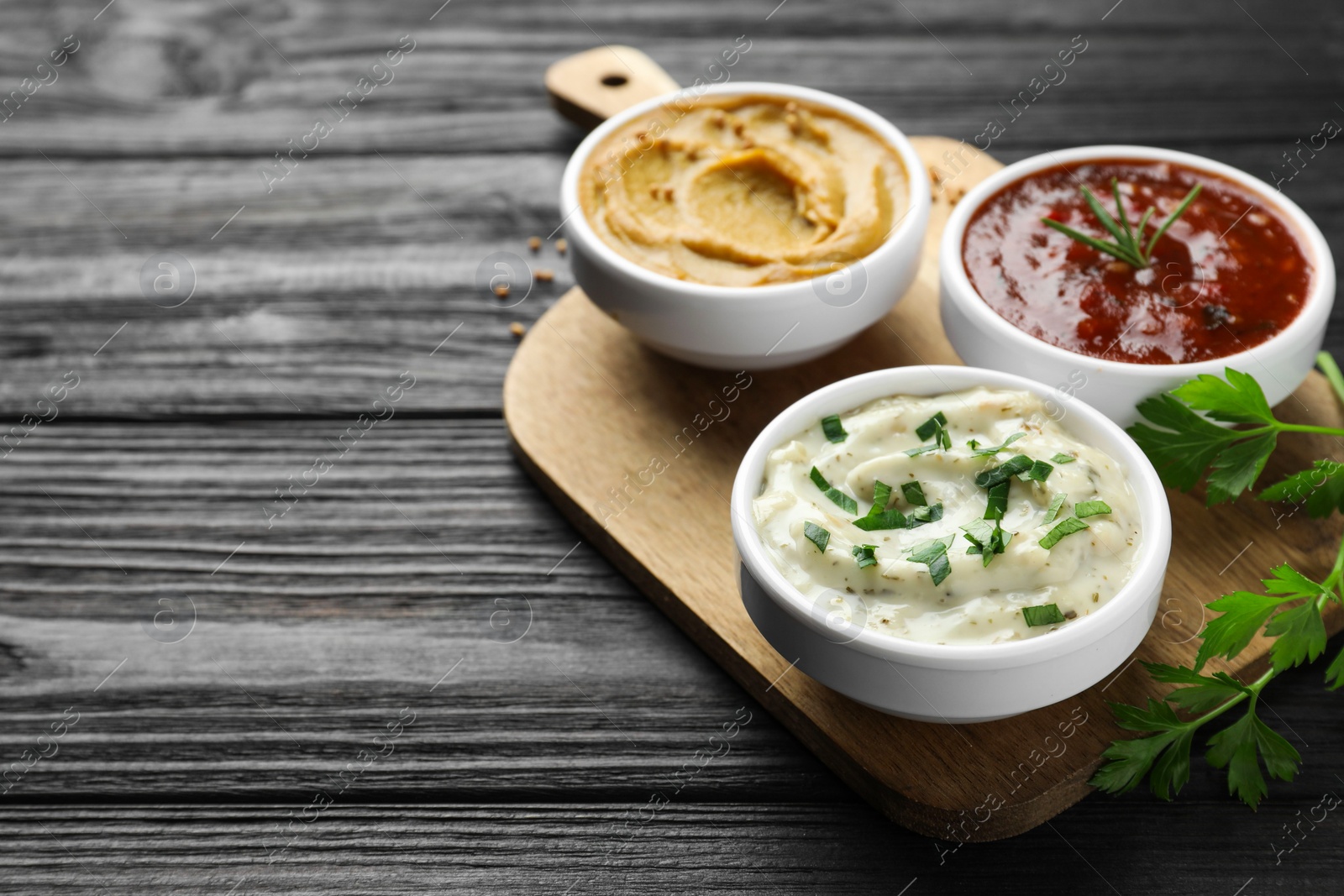 Photo of Different tasty sauces in bowls and parsley on black wooden table, space for text