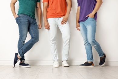 Group of young men in jeans and colorful t-shirts near light wall