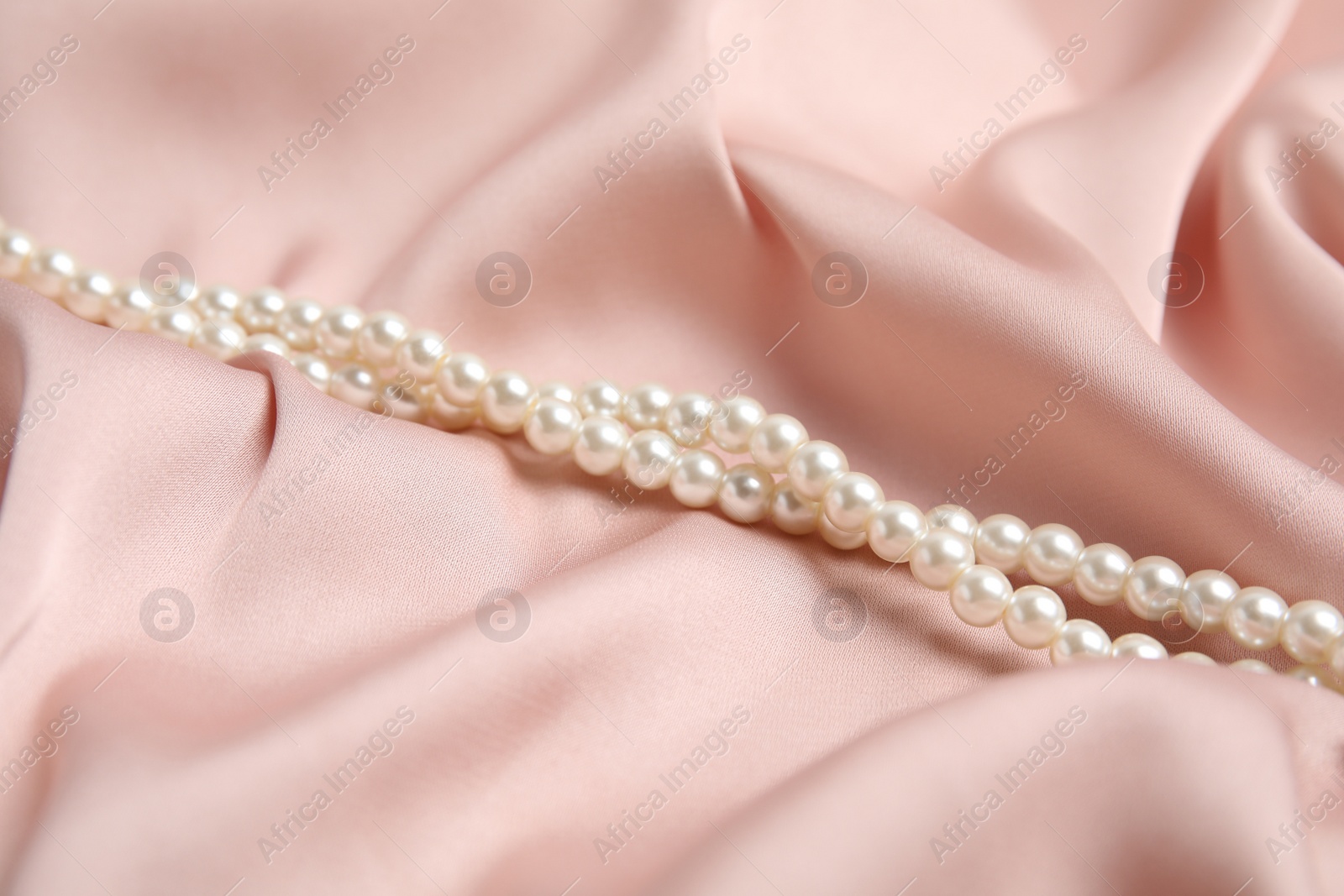 Photo of Beautiful white pearls on delicate pink silk