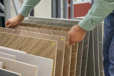 Photo of Man choosing tile among different samples in store, closeup