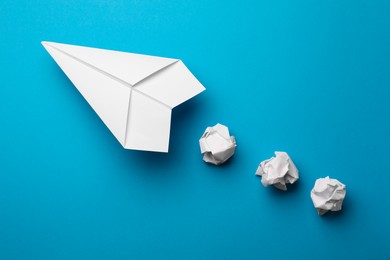 Photo of Handmade white plane and crumpled pieces of paper on light blue background, flat lay