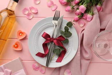 Place setting with heart shaped candles and bouquet of roses on pink wooden table, flat lay. Romantic dinner