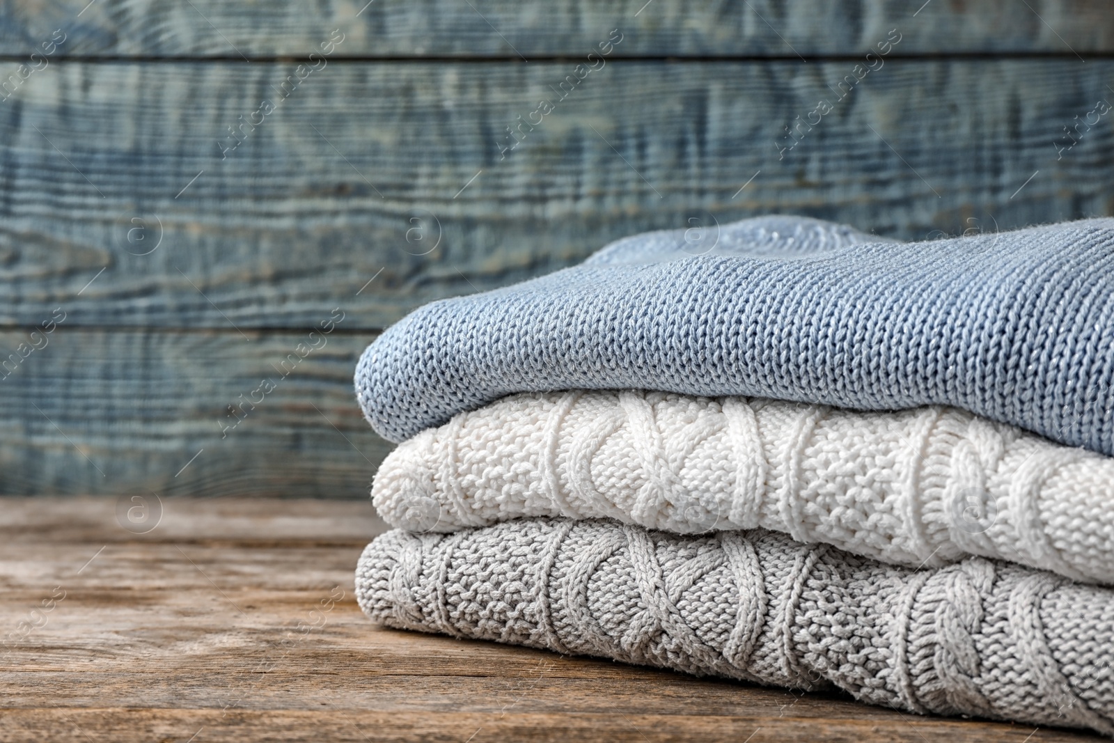 Photo of Stack of folded knitted sweaters on table. Space for text