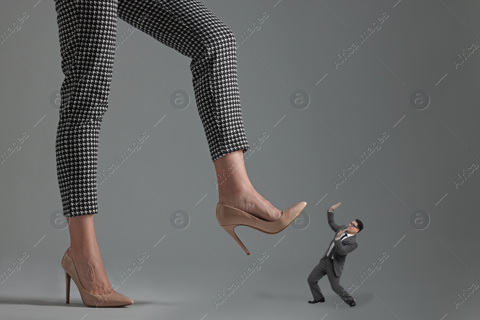 Image of Big woman stepping onto small man on grey background