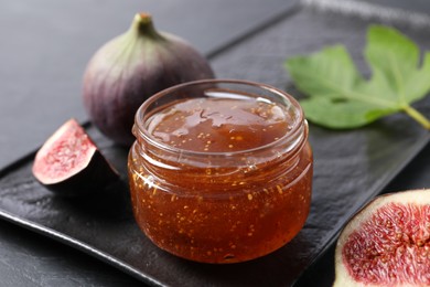 Jar of tasty fig jam and fresh fruits on black table, closeup