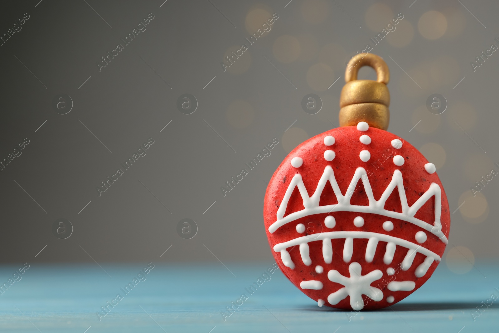 Photo of Beautifully decorated Christmas macaron on light blue wooden table against blurred festive lights, space for text