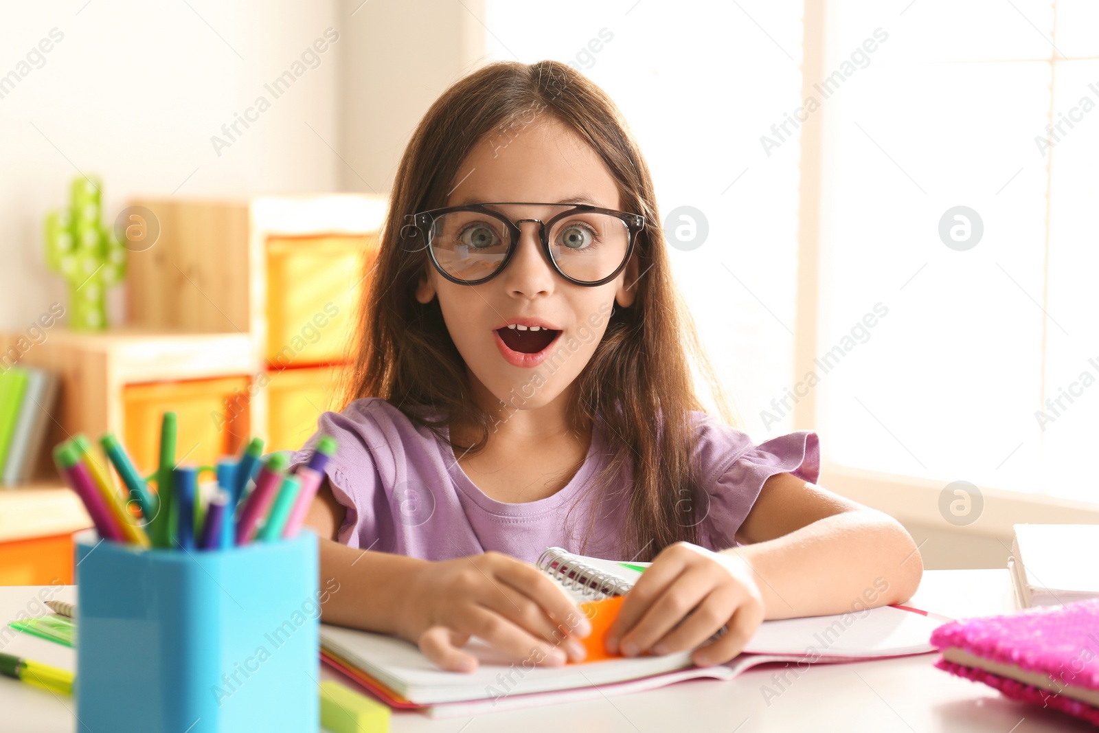 Photo of Emotional little girl doing homework at table indoors