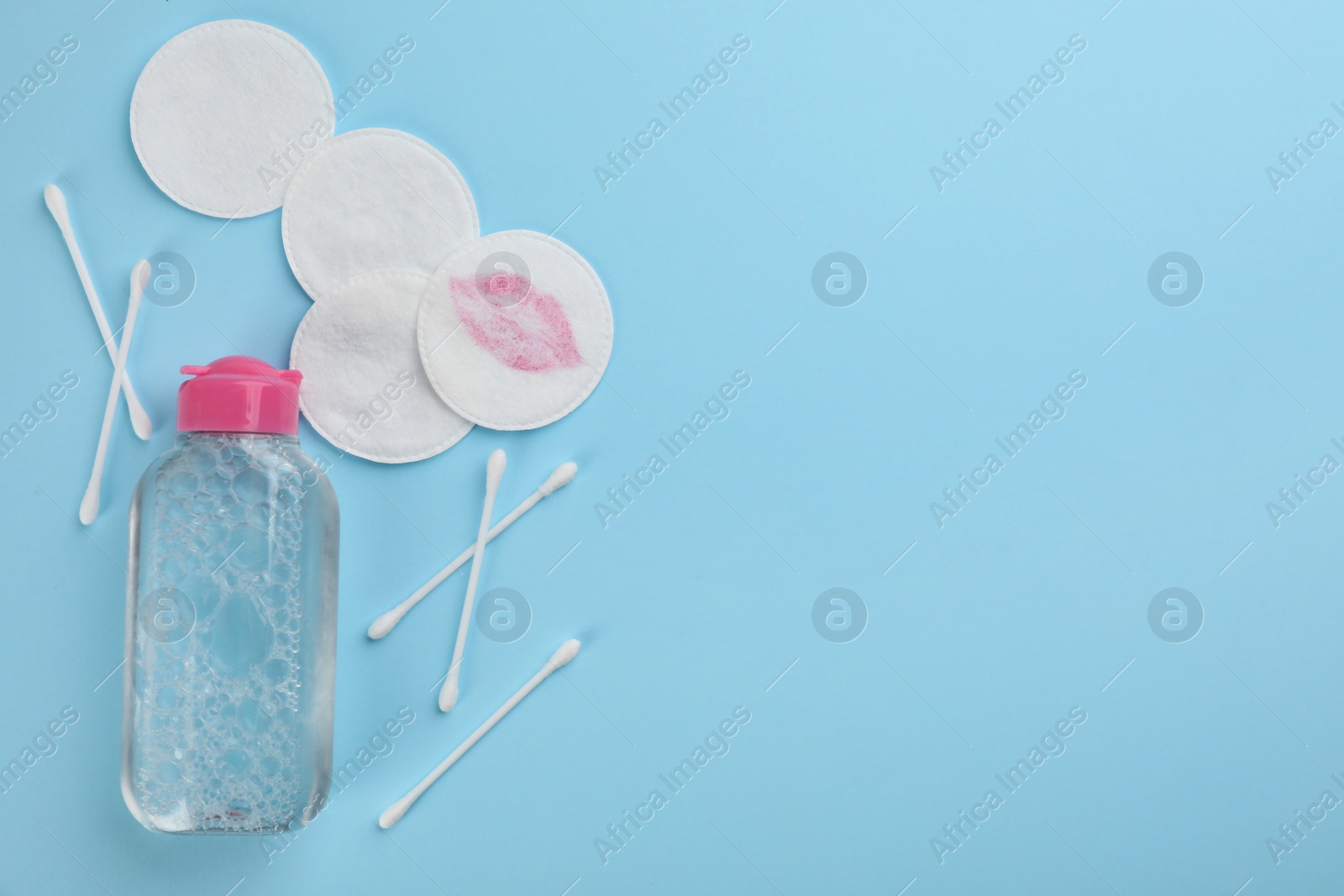 Photo of Dirty cotton pads, swabs and micellar cleansing water on light blue background, flat lay. Space for text