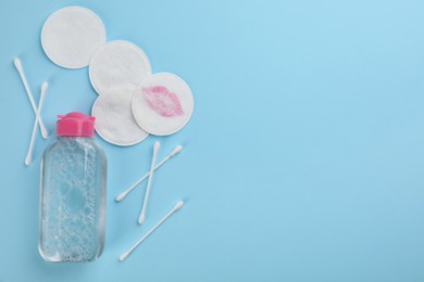 Dirty cotton pads, swabs and micellar cleansing water on light blue background, flat lay. Space for text