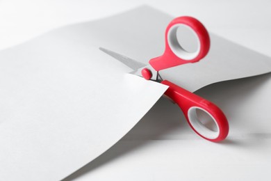 Photo of Red scissors cutting paper on white wooden background, closeup