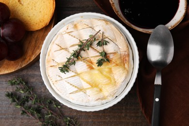 Photo of Tasty baked camembert and thyme in bowl served on wooden table, flat lay