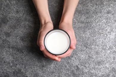 Photo of Woman holding glass of milk at grey table, top view