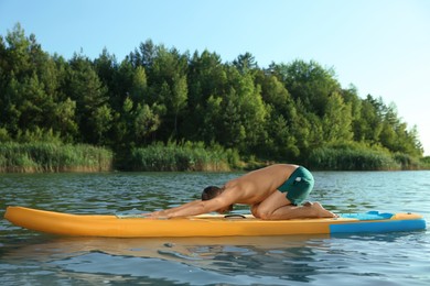 Man practicing yoga on color SUP board on river