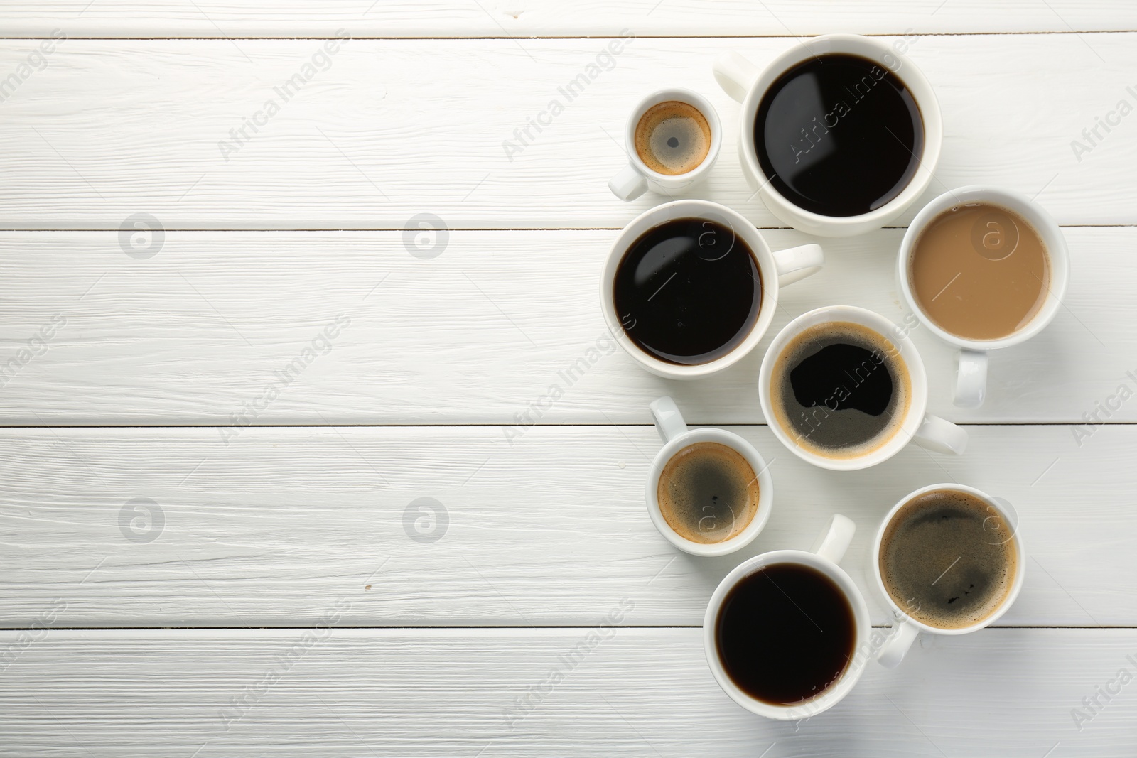 Photo of Different coffee drinks in cups on white wooden table, flat lay. Space for text