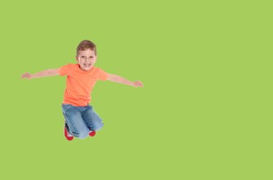 Happy boy jumping on light green background, space for text