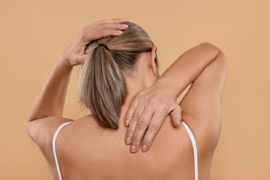 Photo of Mature woman suffering from pain in her neck on beige background, back view
