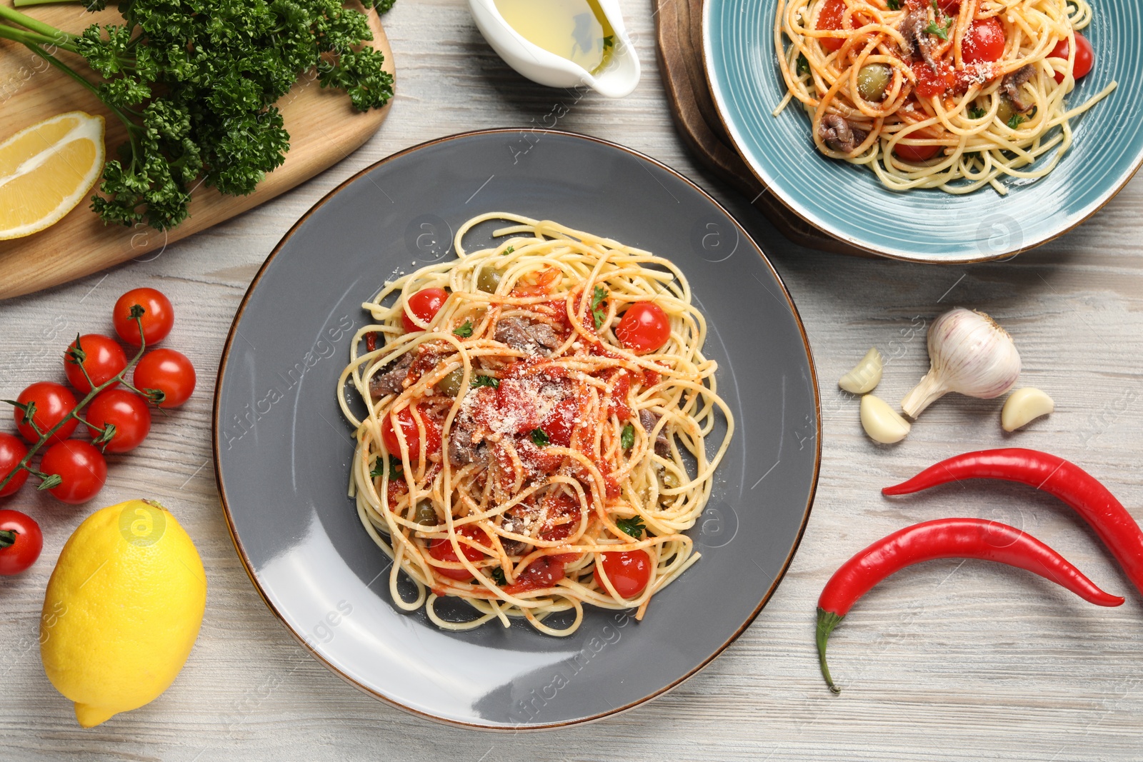 Photo of Delicious pasta with anchovies, tomatoes and parmesan cheese served on white wooden table, flat lay